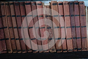 Old books in a row with unnamed spines and ragged covers on a shelf