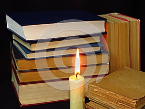 Old books stacked in a pile and a burning candle.