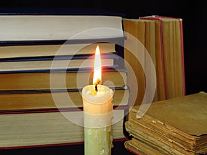 Old books stacked in a pile and a burning candle. Education, knowledge, reading habits, paper, library, light, flame, mystery.