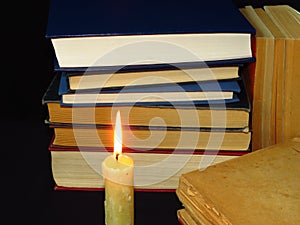 Old books stacked in a pile and a burning candle. Education, knowledge, reading habits, paper, library, light, flame, mystery