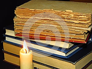 Old books stacked in a pile and a burning candle. Education, knowledge, reading habits, paper, library, light, flame, mystery.