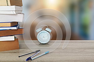 Old books, textbooks,blue classic alarm clock and pens on vintage wooden table on blurred room background