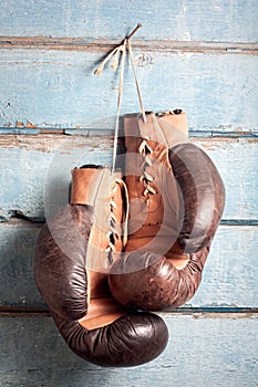 Old boxing gloves with a lace over blue wall