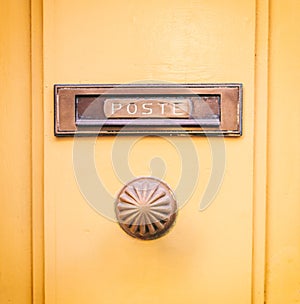 Old brass mail letter box and knob on a yellow painted front door, text poste photo