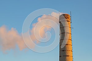 an old brick chimney of a factory boiler room with smoke on a blue sky background