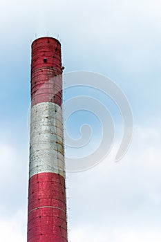 Old, brick factory chimney painted white and red against blue, cloudy sky