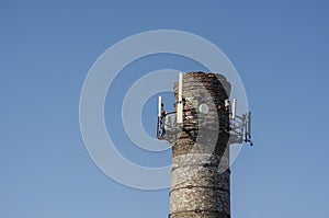 An old brick factory chimney with various antennas