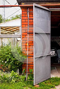 Old brick garage with an open door. There is a ladder propped up against the garage