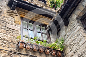 Old brick house in the village. Facade of medieval building with flower pots. Checkered window, roof tiles and exterior decor.