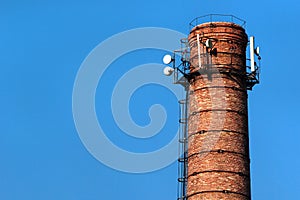 Old brick pipe with antennas against blue sky background