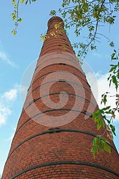 Old brick pipe factory against a blue sky and green leaves.