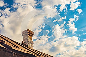 An old brick pipe on the roof of a residential building with an iron roof against a background of clouds, HDR