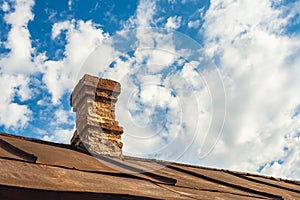 An old brick pipe on the roof of a residential building with an iron roof against a background of clouds, HDR