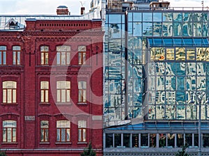 An old brick residential building and an adjoining modern office building with solid glazing reflecting the elements of the street