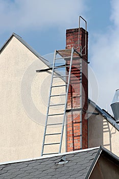 Old brick smokestack on a rooftop with a metal ladder for servicing