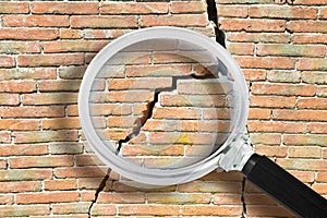 Old brick wall cracked and damaged with a diagonal deep crack- Concept image seen through a magnifying glass