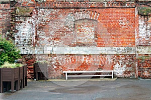 Old brick wall with a laid window next to a bench made of white wood and plants in stands