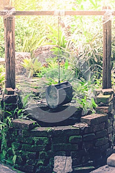 Old brick water well with bucket hanging on timber in the garden.