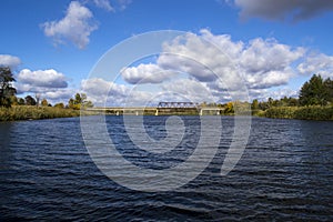 Old bridge across the river with autumn trees and beautiful clouds. Travels. Fishing