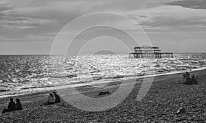 The old Brighton pier in black and white, people chilling on the beach.