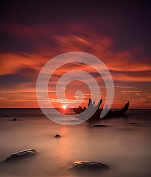 Old broken boat wreck on the shore, a frozen sea and beautiful blue sunset background.