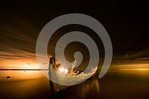 Old broken boat wreck on the shore, a frozen sea and beautiful blue sunset background.