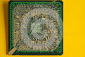 An old broken computer CPU with a torn chip on a yellow background