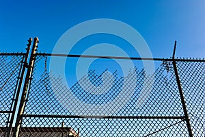 Old broken cyclone fence against blue sky