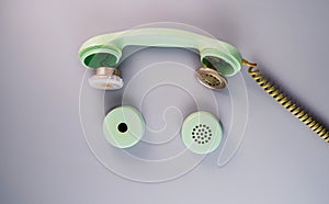 An old broken green telephone receiver with twisted cord on a gray background. Vintage untwisted telephone receiver