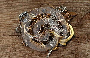 Old and broken jewelry, watches of gold and silver on a wooden texture.