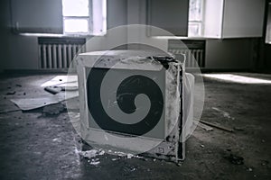 An old, broken monitor lies on the floor in an abandoned building. Sunbeams in the windows in the background.