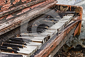 An old broken piano thrown into the street with peeling paint and leaves on the keys