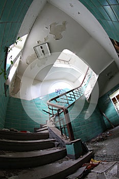 Old broken staircase with turquoise tiles, stone stairs and metal railing with wooden handrail. Several floors house.