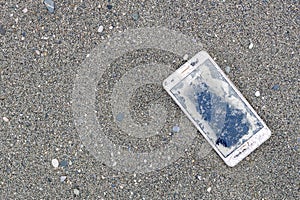 Old broken white smartphone lying on the sand