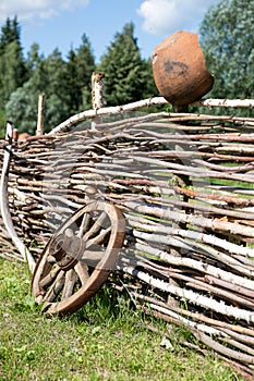 Old broken wooden carriage wheel on wattled fence