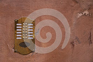 Old bronze intercom on an old wall with peeling paint.