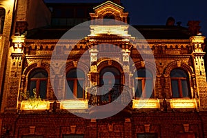 old brown brick house with windows and a balcony with lighting on the night street