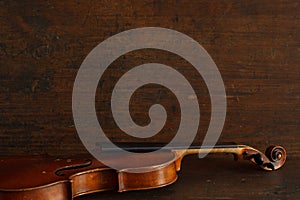 Old brown broken violin without strings lies on brown antique wood background