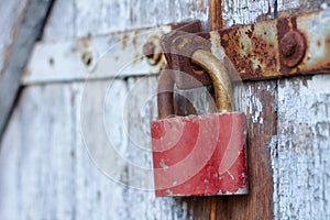 Old brown padlock on a gray door with wooden planks of cracked paint and rust. Vintage gates with metal stripes and bolts