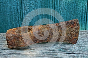 Old brown rusty battle ax on a gray board at the green wall