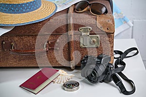 Old brown vintage suitcase with straw hat, photo camera, sunglasses, passport and a map, travel and summer vacation concept, copy