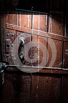 Old brown wooden door locked with a padlock and illuminated by a lamp. Spooky door in the dark