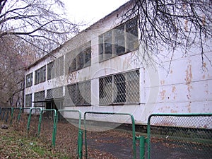 The old building of an abandoned school behind a fallen fence emptied in the fall idle