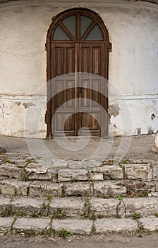 An old building with an arched wooden door and a stone ruined staircase