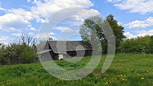 The old building, a barn with a slate roof, stands on a grassy lawn with dandelions in a rural setting. Behind the old boardwalk f