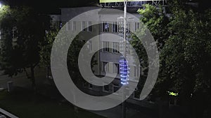 Old building illuminated by lanterns in modern night city. Stock footage. Top view of lighted old building in center of