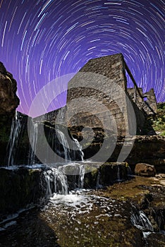 Old building in ruins next to a waterfall with the night sky in the background