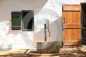 Old building with shutter window, vintage antique water pump and wooden door.