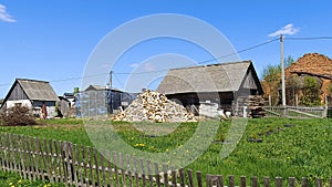 An old building, a wooden barn with a slate roof, stands on a grassy lawn with dandelions in a rural setting. Behind the old board