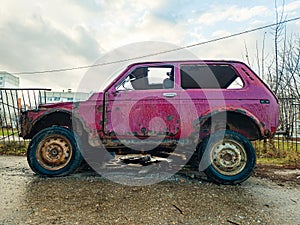 Old burnt-out car is red. An abandoned car against the background of gray panel houses